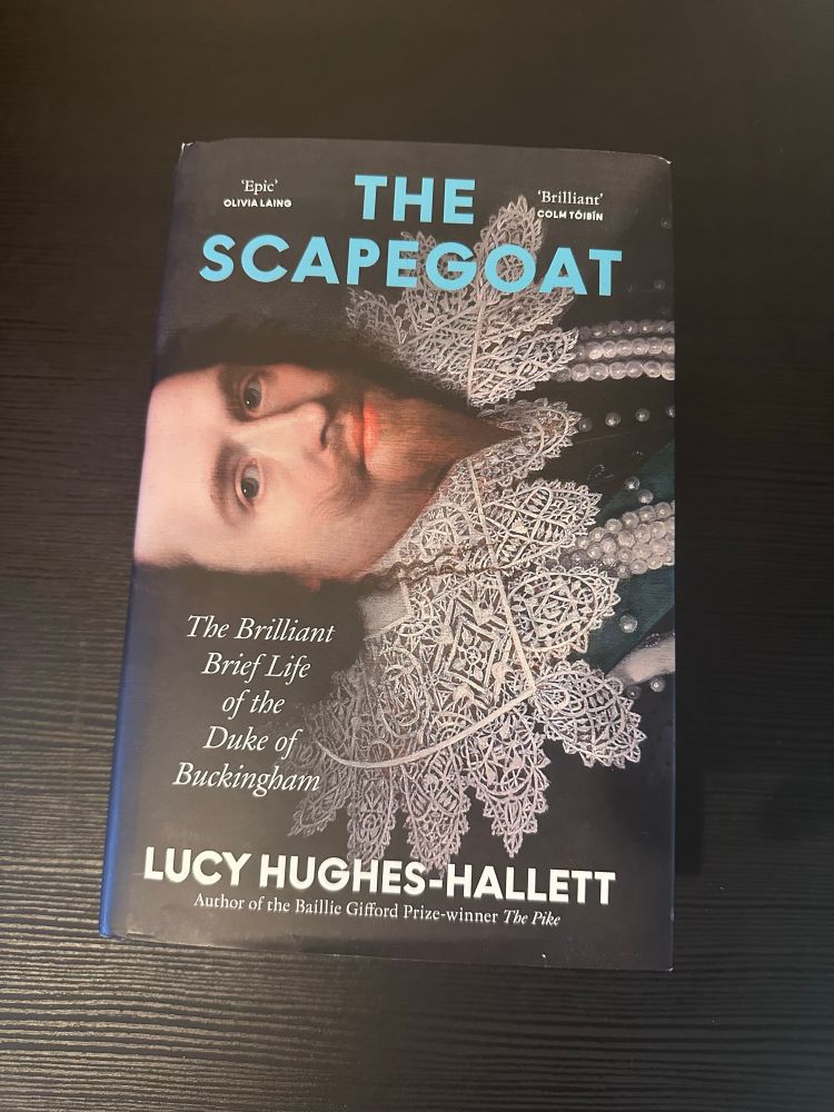 Book cover of 'The Scapegoat: The Brilliant Brief Life of the Duke of Buckingham' by Lucy Hughes-Hallett. The cover features a historical portrait showing part of George Villers (the Duke) face. The title appears in light blue text at the top, with the author's name in white at the bottom. There are also review quotes from Olivia Laing calling it 'Epic' and Colm Tóibín calling it 'Brilliant' at the top of the cover. The book notes that Hughes-Hallett is the author of the Baillie Gifford Prize-winner 'The Pike'