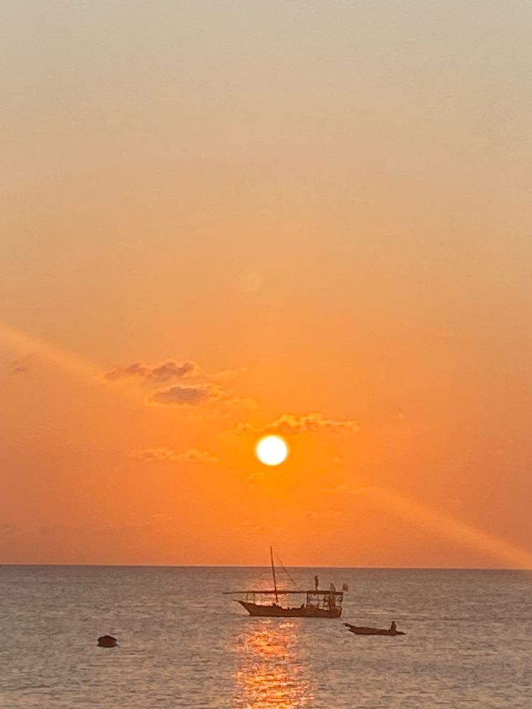 A larger and smaller boat on the ocean with the sun setting creating an orange sky 
