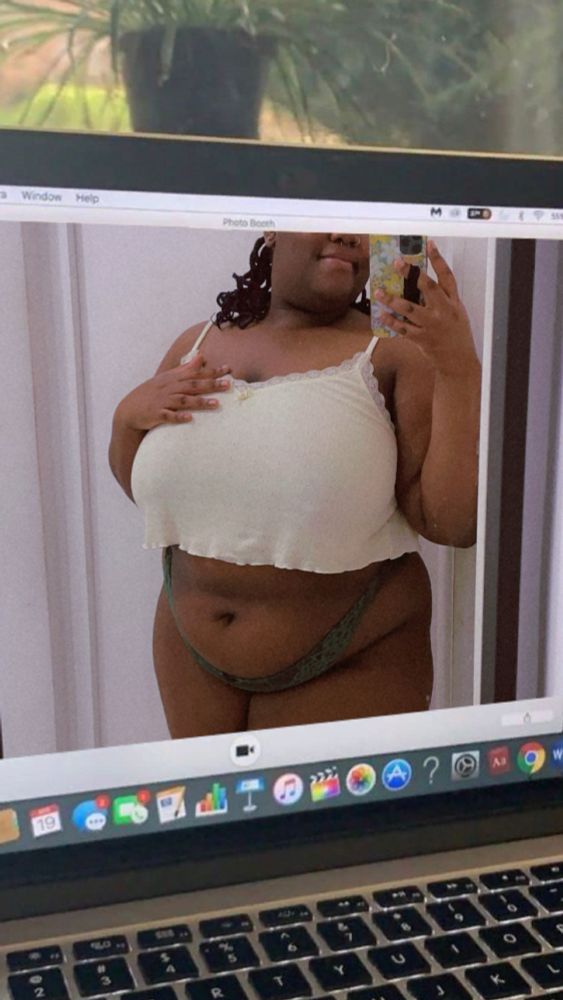 sunny is seen on a fake laptop screen posing in the mirror. she’s wearing a cropped pale yellow vest and dark green lacy panties, with their hand resting on their chest.