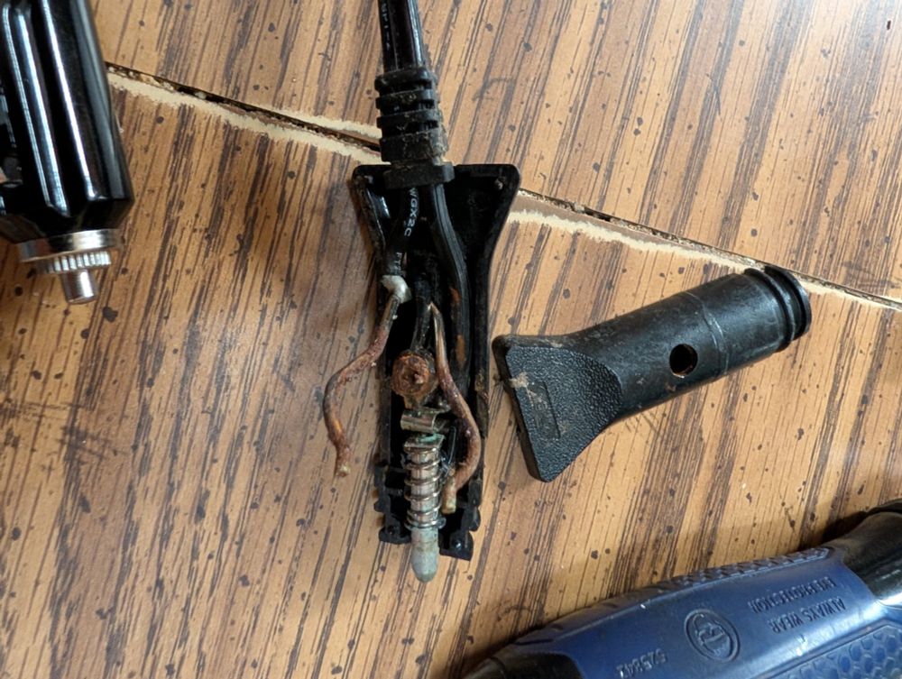 A close-up of the old, faulty car accessory plug after being cracked open to assess the wiring's polarity. The heavily corroded and rusty internal contacts are exposed, showing how the original wires were connected before they were removed.