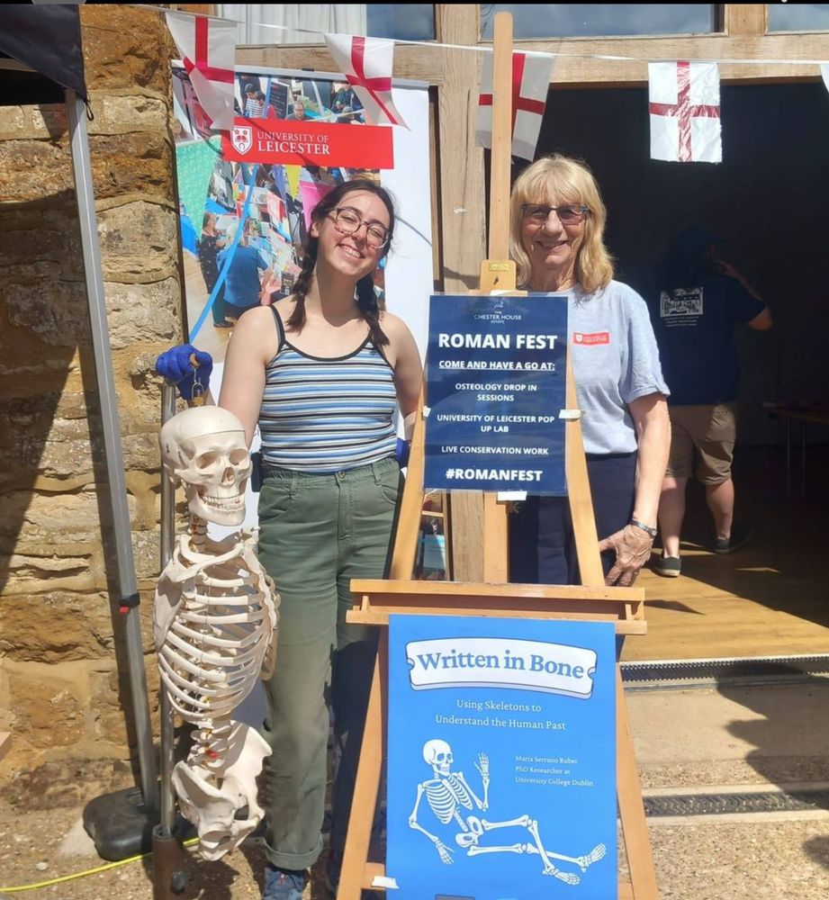 Maria and Jill standing by a plastic hanging skeleton, and behind a sign advertising an osteology drop-in session at Chester House Estate's Roman Fest event. 