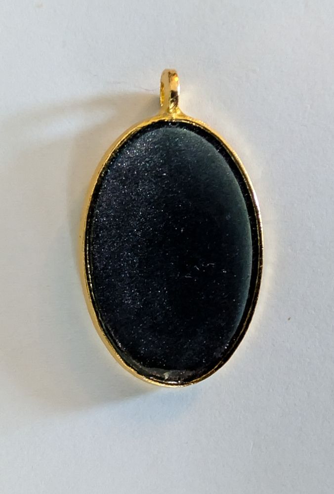 Image of an oval pendant, on a white background, the colour is black, sort of glittery on one side.