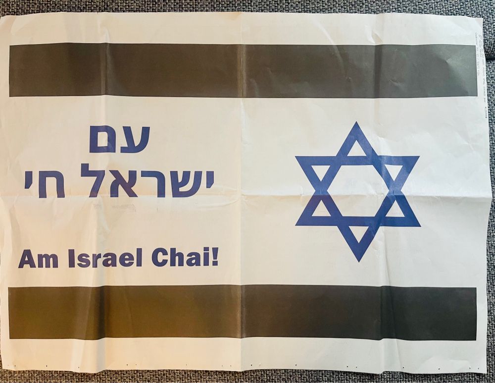 A fullsized flag of Israel with black stripes instead of blue and the text Am Israel Chai in Latin and Hebrew letters.