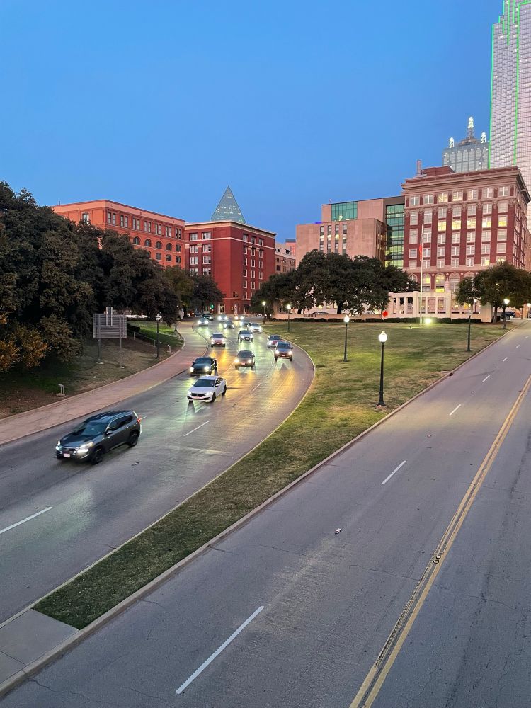 A photo of Dealey Plaza from the Triple Underpass. Cars are driving down Elm Street and the Texas School Boom Depository is in the background 