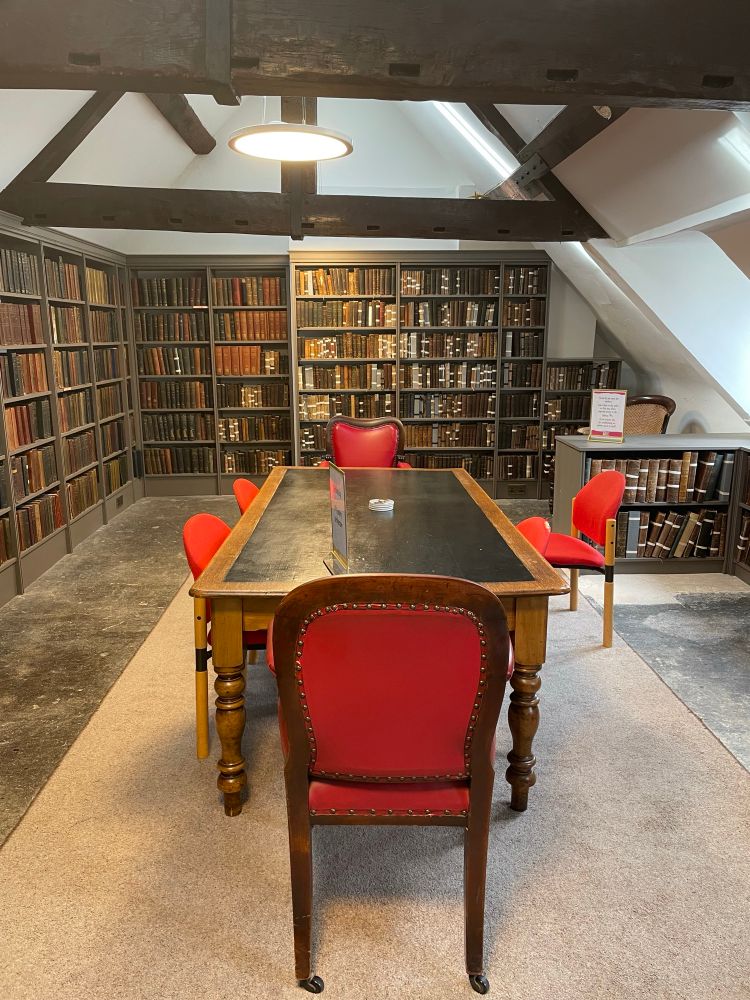 Studded red leather chairs, around a long table, in a room lined with old books 