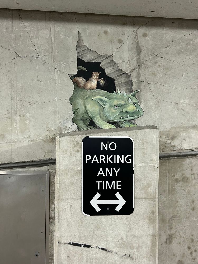 Chalk drawing of gargoyle with squirrel on its back above a no parking anytime sign in an underground parking garage 