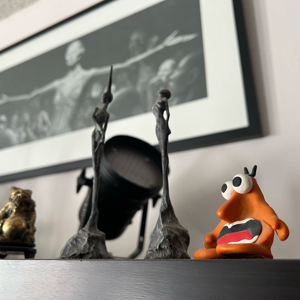 Shelf with figurines with a white wall and art in the background. 