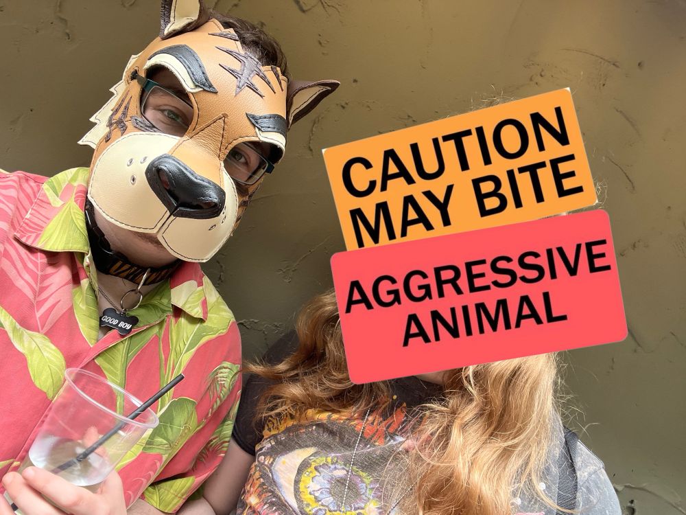 a selfie of me in my pup hood with my partner, whose face is covered by the text “caution may bite / aggressive animal”