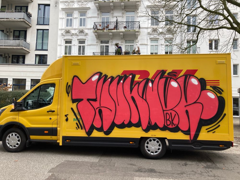 DHL-truck with big graffiti letters on the side. The word is „THUndeR“ in red letters with black outlived and a drop shadow to the down right. In the right top corner of the letters the artist set white highlights. On the outside of the word are some lines indicating wobbly movement. In the lower part of the „e“ sits the signature B.K. written in black.