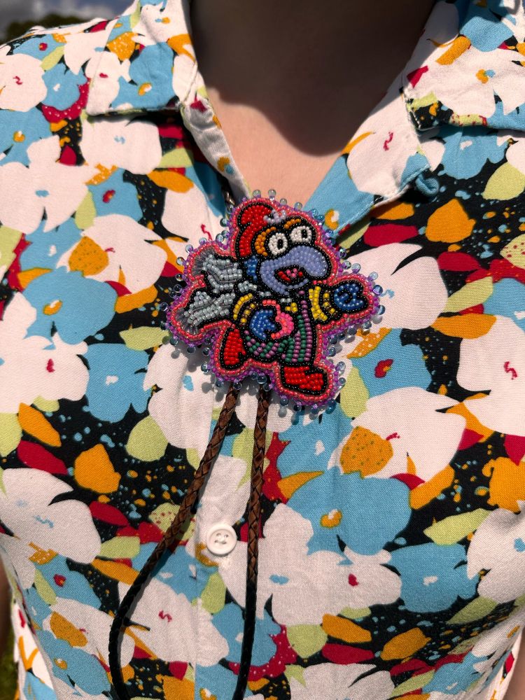 Beaded gonzo bolo tie being worn on top of a colorful floral shirt. Gonzo is wearing colorful clothing and a hat/scarf