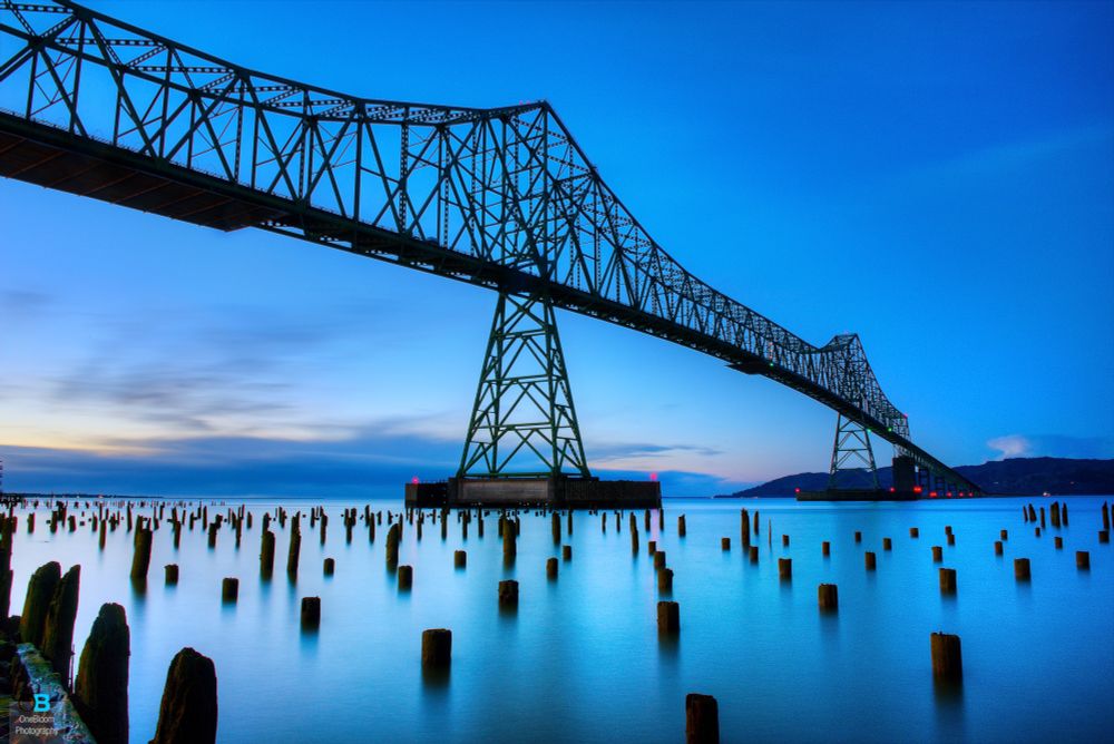 Blue hour sunset long exposure of the Astoria-Megler Bridge from a low angle with the old piers poking out of the water.