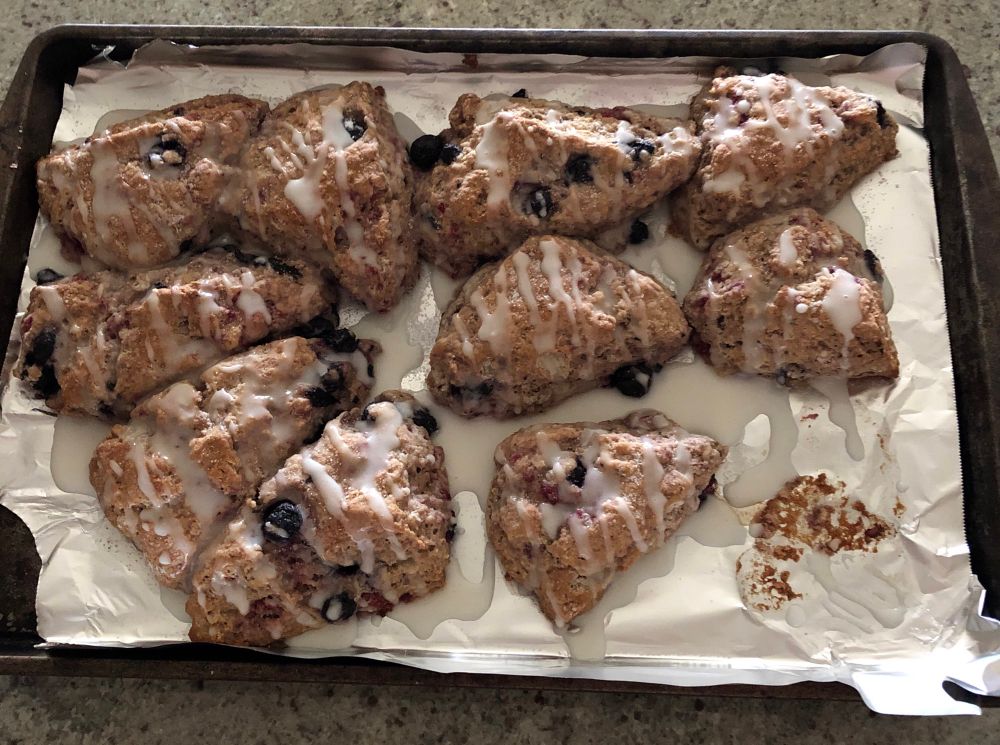 Oblong triangular blueberry and raspberry scones with lemon icing drizzled over the top. They are slightly smushed together on the cookie sheet because somebody can’t eyeball spacing well. 
