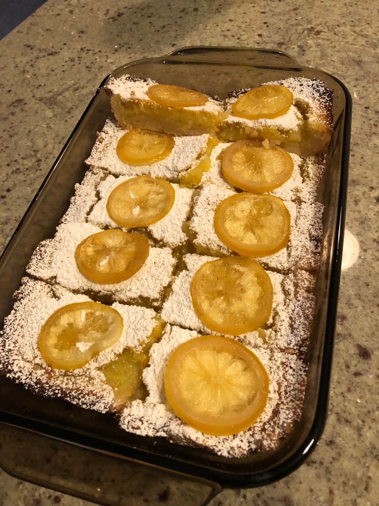 A pan of lemon bars topped with powdered sugar and candied lemons. 