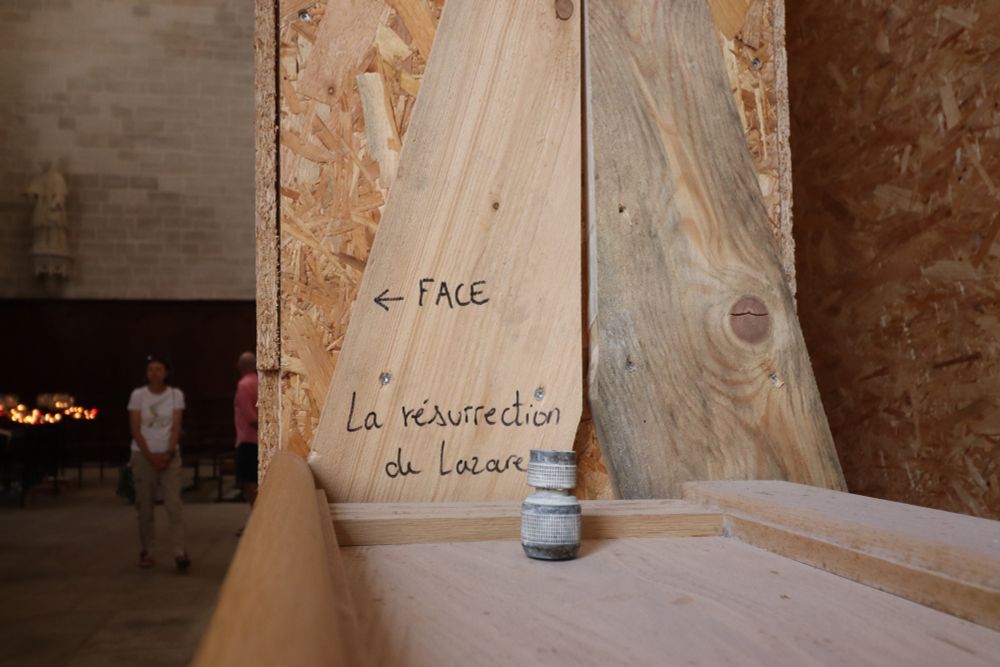 In einer Kirche mit Bauarbeiten. Eine große Kiste aus OSB-Platten, beschriftet "La resurrection de Lazare". Links ein Gestell mit Opferkerzen.