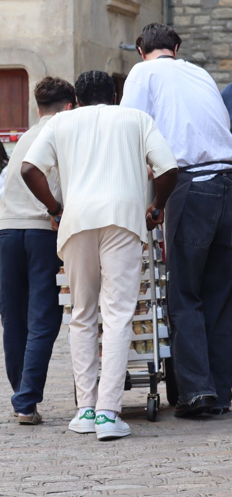 Drei junge Männer schieben einen Wagen beladen mit Senfgläsern über holpriges Straßenpflaster
