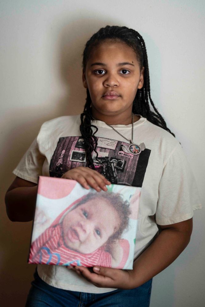 Ja’miya, daughter of Shakenya Griffin, stands for a portrait holding a baby photo of her little brother Ramone “Red” Luckie Carter in Buffalo, Jan. 23, 2025. Ja'miya and Ramone were playing outside with other children on June 21, 2024 when they were struck by gunfire. Ja'miya survived her injuries, but Ramone did not. (Libby March/Buffalo News)