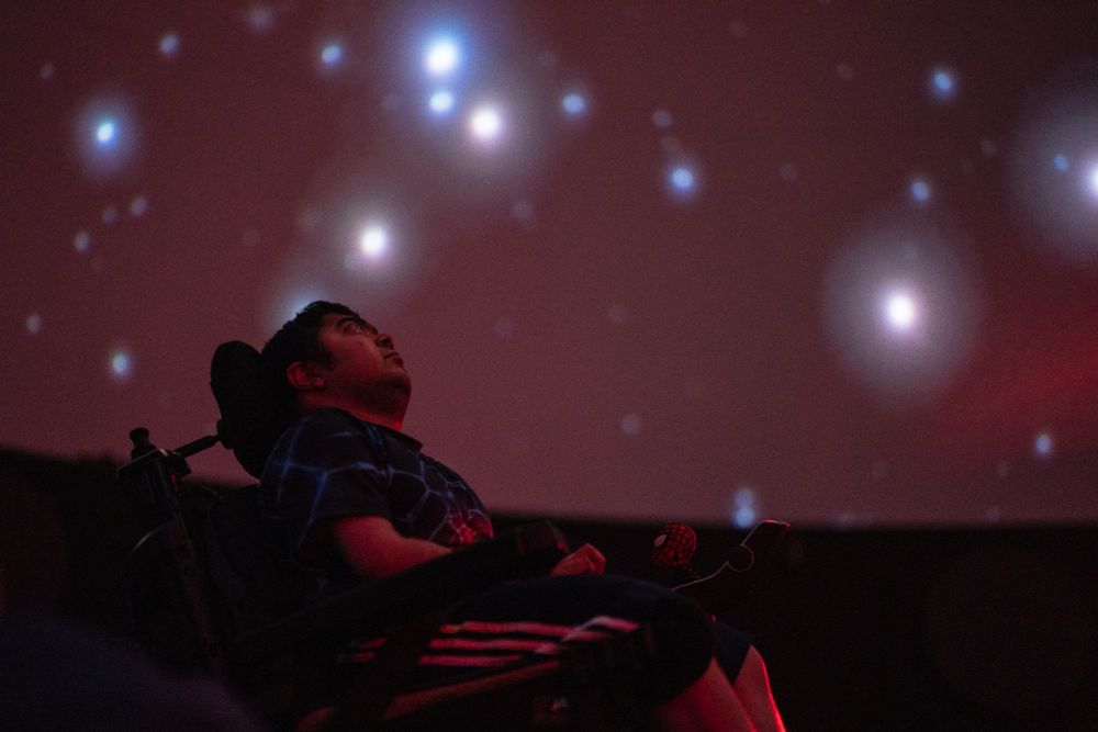 Suneel Ram gazes up at galactic photographs seen at the planetarium inside the EcoTarium in Worcester, Mass., June 12, 2024. After eight hours of travel the day before and a full day of medical appointments in Worcester, Suneel was eager to make it to the planetarium show, which was not playing when they tried to see it during last year’s excursion to Worcester. (Libby March/Buffalo News)