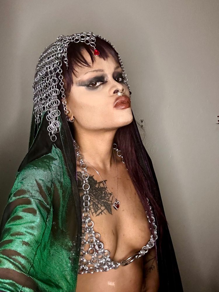 Selfie, Mina is dressed in a chainmail headdress and bra with a sheer cape and smeared black eyeliner