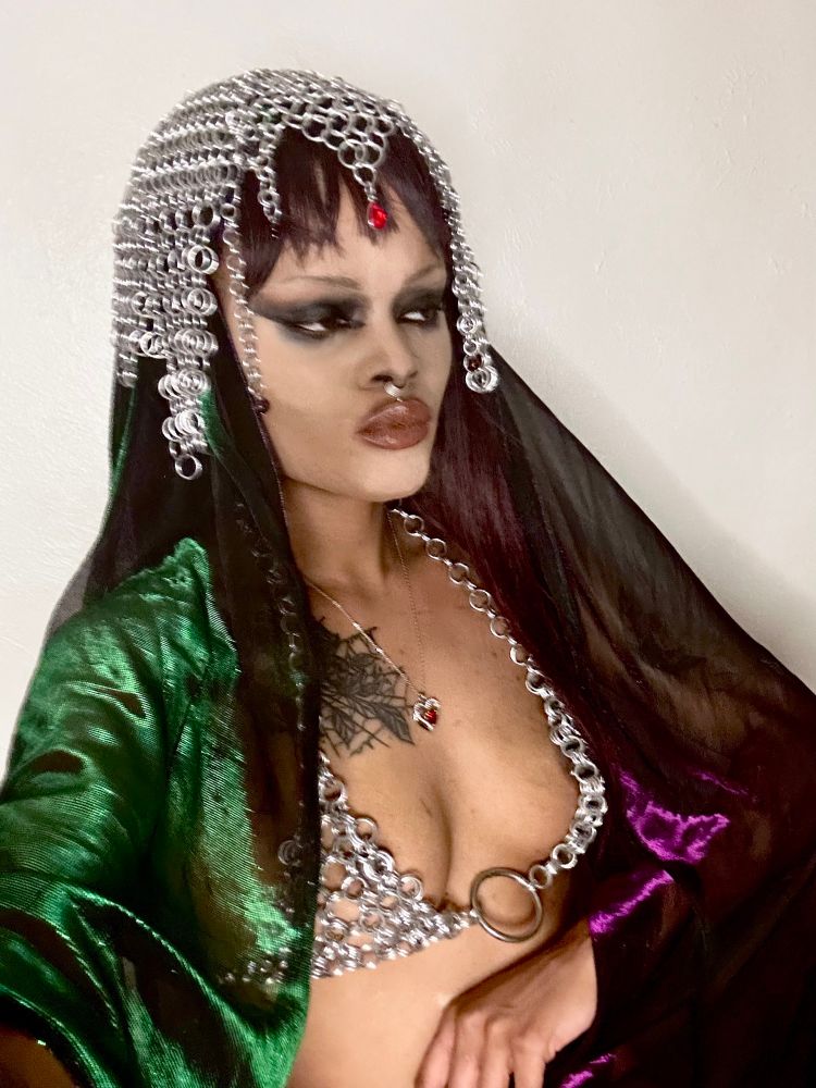 Selfie, Mina is dressed in a chainmail headdress and bra with a sheer cape and smeared black eyeliner