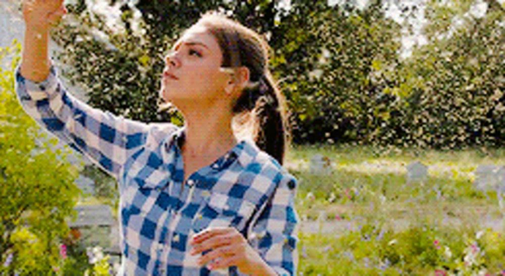 a woman in a plaid shirt is standing in a field of flowers looking up .