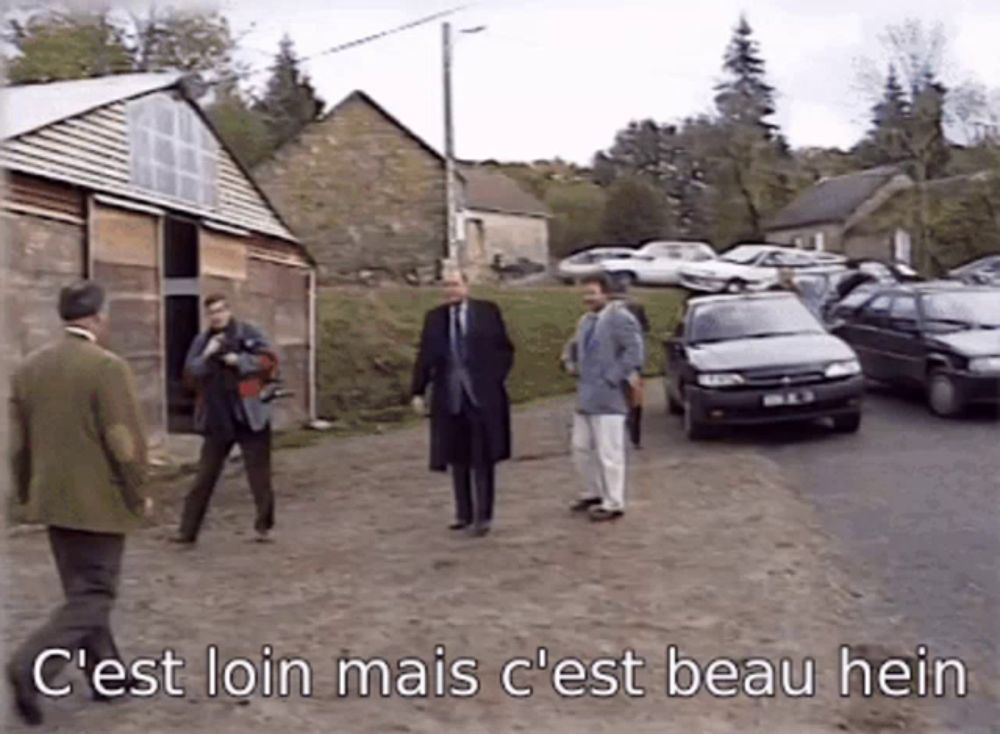 a group of men are standing in a parking lot with the words c'est loin mais c'est beau hein written below them