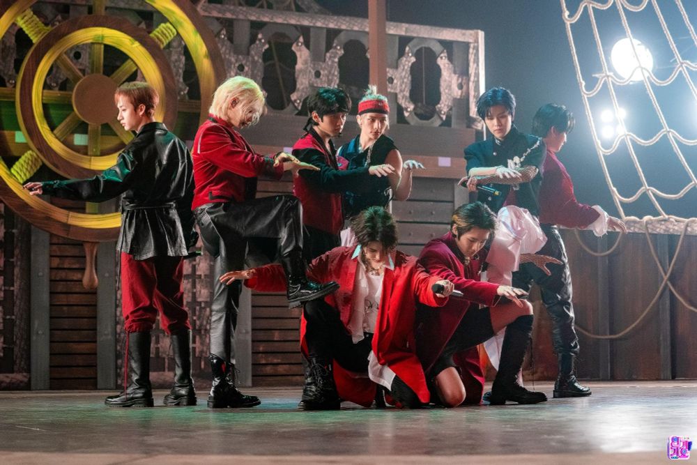 stray kids on stage with a pirate ship set in red & black pirate outfits, performing their song lalalala