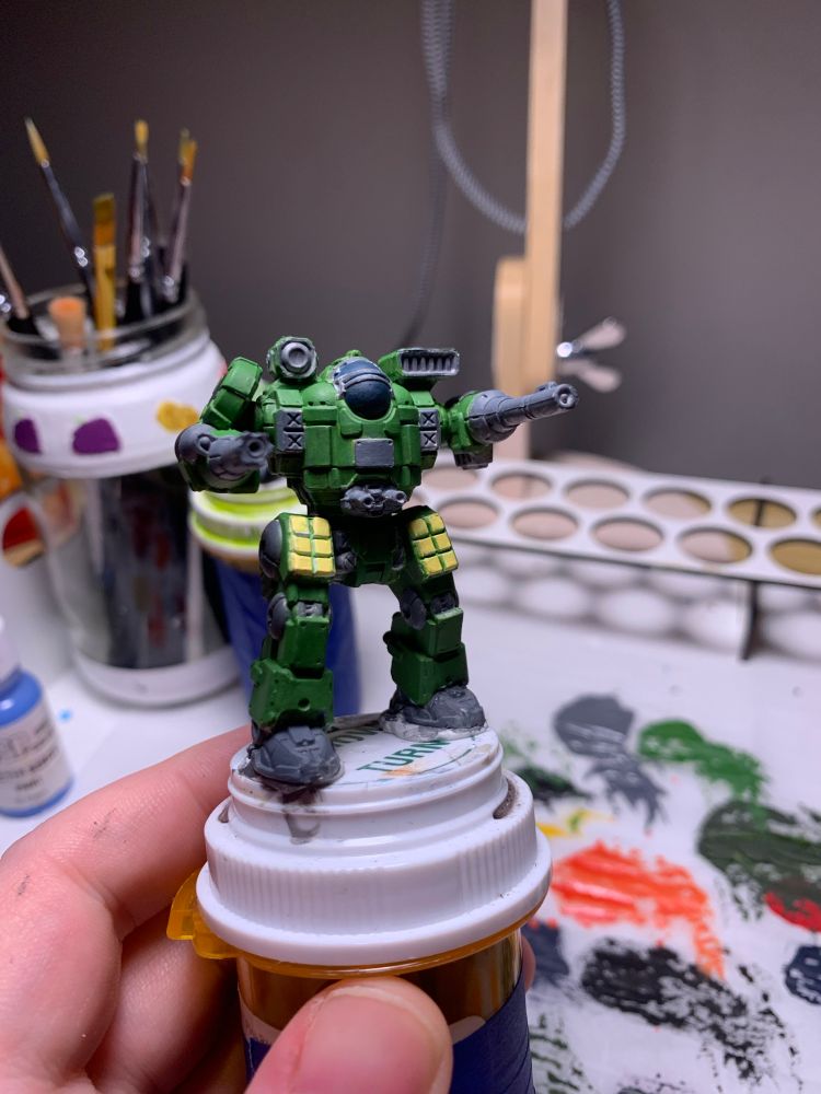 a bright forest green mackie from battletech. the weapons, joins, and some plates of armor are painted a deep gray. the thighs are painted a bright yellow, to mimic explosive armor. the cockpit is currently painted a deep blue