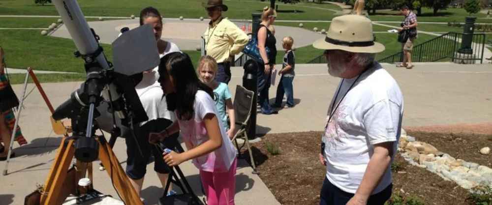 A volunteer of the Denver Astronomical Society stands by as children take turns viewing the Sun through a solar telescope.