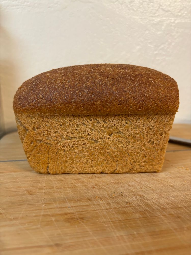 A loaf of whole-grain sourdough bread, sitting on a cutting board, missing one end piece. 
