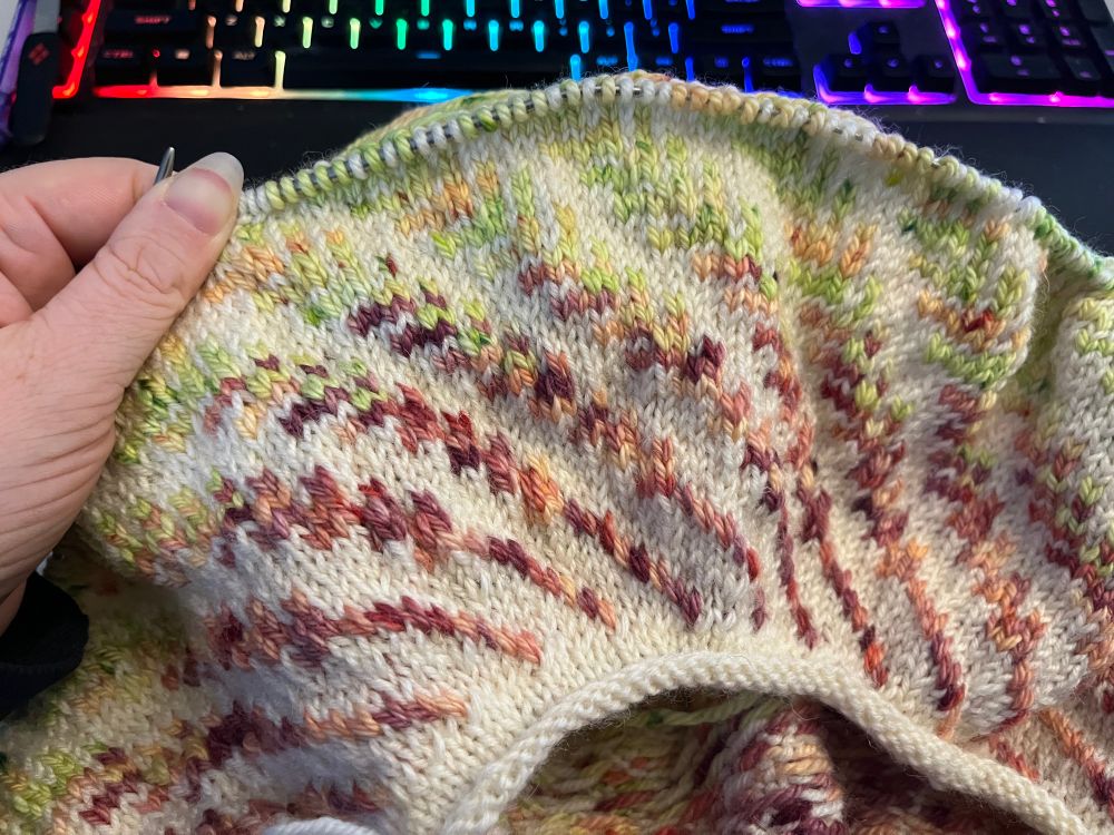 The yoke of a sweater with pink and green fern fronds curving around it.