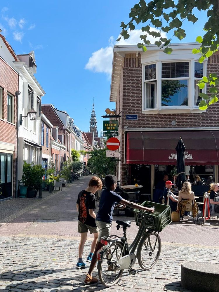 two kids, one pushing a bike, on a woonerf in Haarlem. grown ups sitting at a bar.