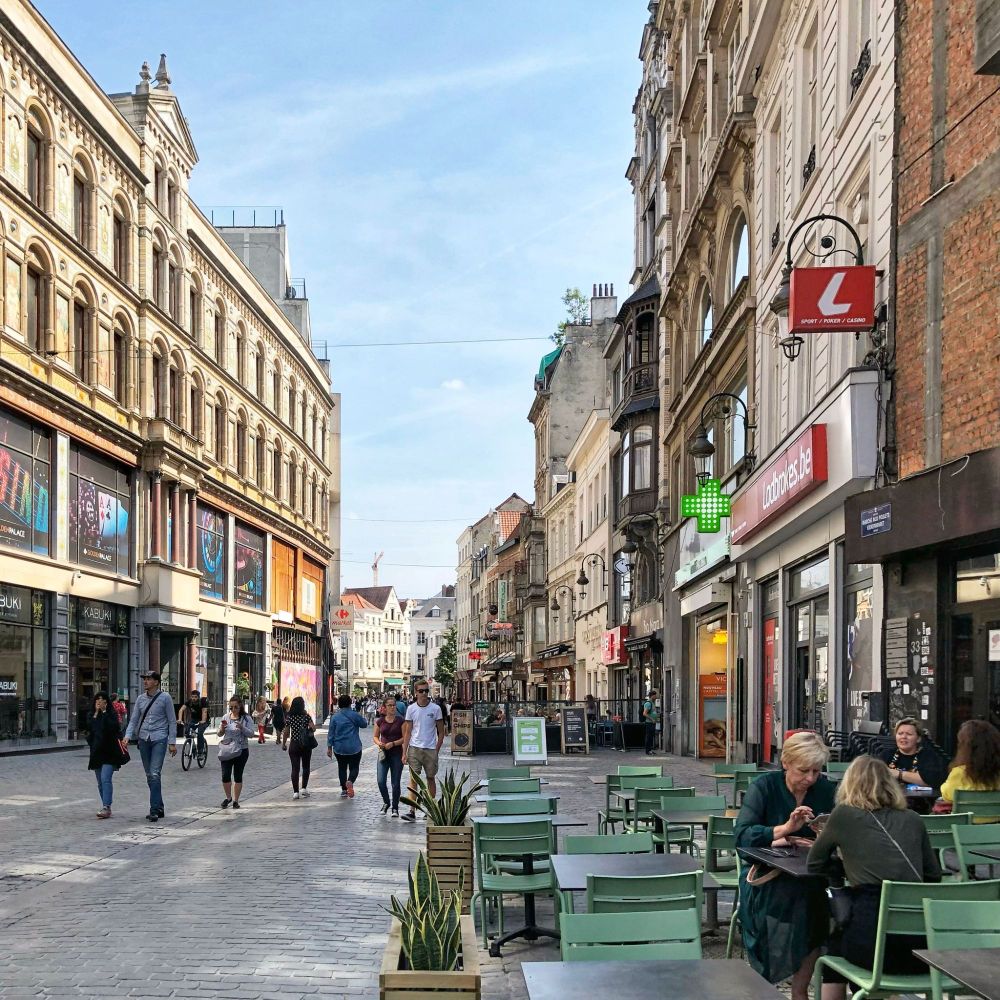 Exact same street photographed by me. Now it has been transformed to a pedestrian street. There are tables and chairs and people walking and biking. There are no more cars. Also a sunny day.
