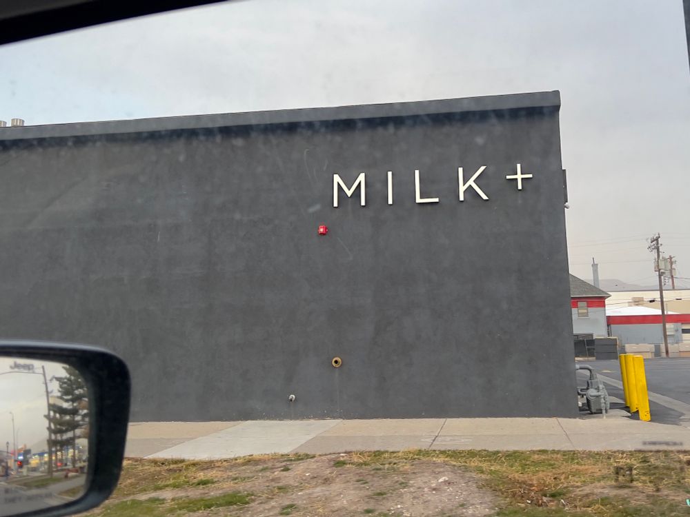A featureless grey building with a sign that reads MILK+