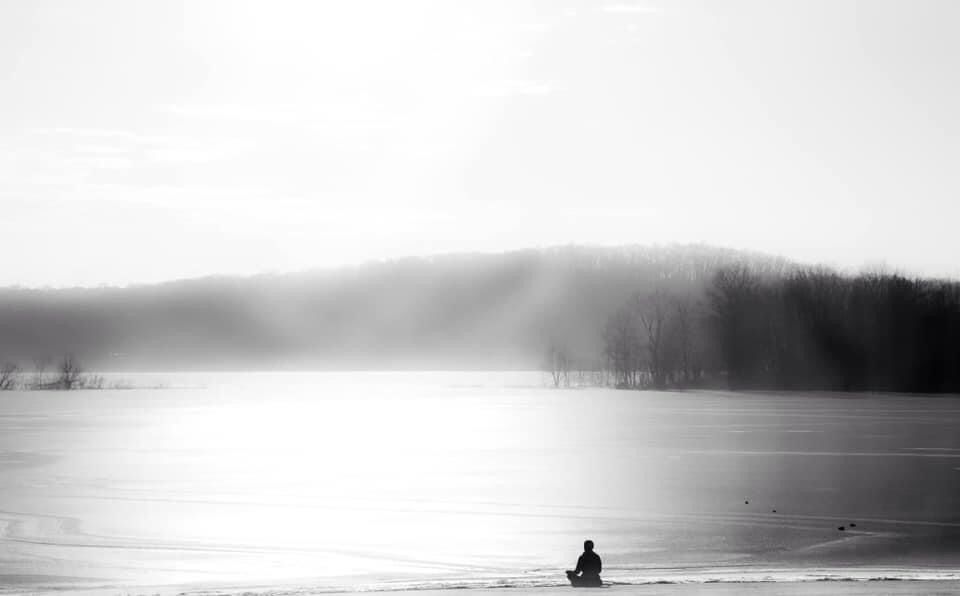 Woman sitting in meditation on shoreline of lake.  Light of the sun and spiritual enlightenment. 