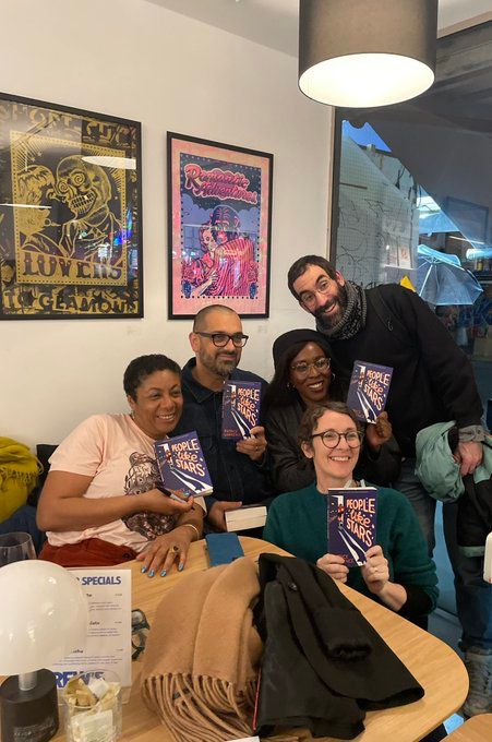 A group photo at the launch. 5 people are sat or stood around a sofa. All hold up a copy of People Like Stars and are smiling, off to their left. Patrice is sat far left side. Includes Darren Chetty, Sophie Anderson, Adam Ferner and ?- all are authors. 