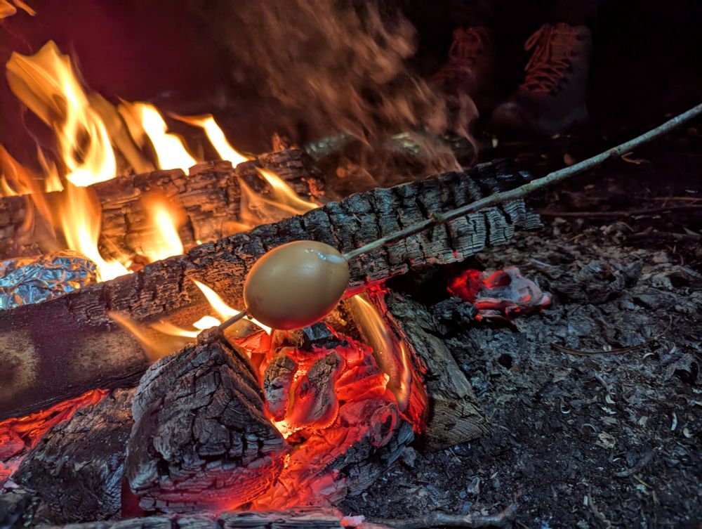 An egg with a thin stick stuck through it and held over glowing embers of a wood fire. 

The trick is to gently tap the shell many times with a knife until the shell breaks but the membrane inside it doesn't. You then need a sharpened and cleaned green stick about 4mm in diameter to stick through the egg and put over the hottest part of the fire quickly so that the white starts to congeal, which will seal the egg while the rest of the inside cooks. 