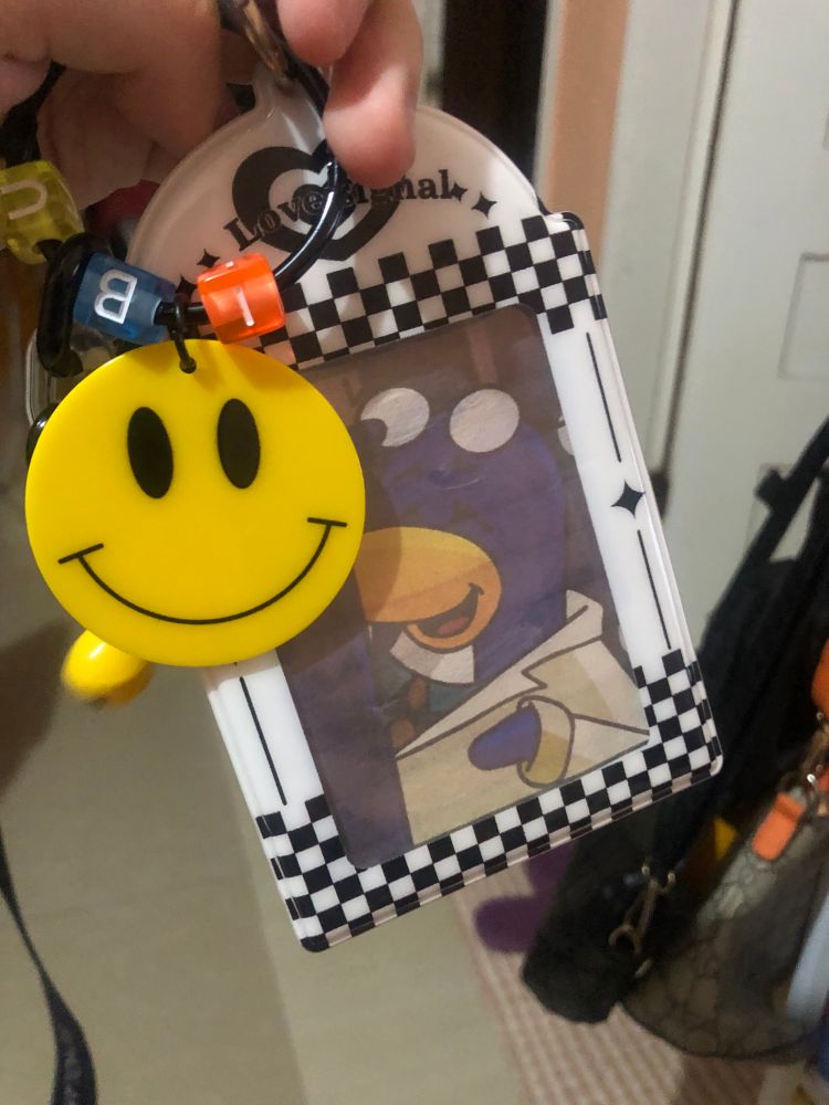 A black and white checkered ID holder with a smiley keychain; inside it being a picture of Gary the Gadget guy but with glasses on his head