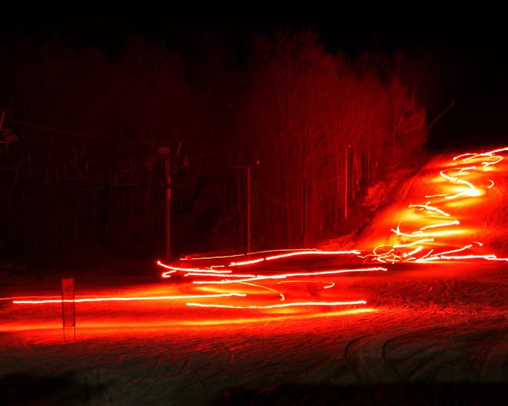 A long-exposure image of a ski slope illuminated by streaks from red flares during a New Year’s Eve “torchlight parade”