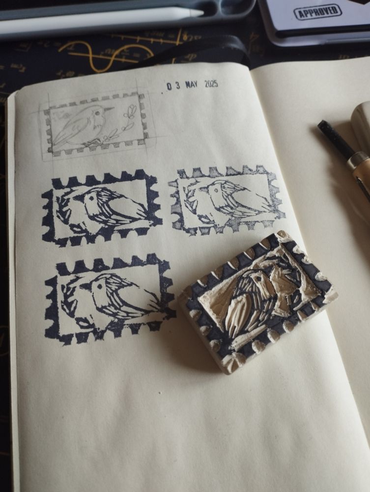 Una hoja de un cuaderno con el diseño original y varias pruebas de estampados. Al lado, el sello, hecho con una goma Milán tallada. El diseño imita un sello y tiene un petirrojo con una ramita 