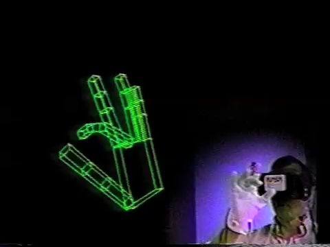 wireframe model of a hand viewed from a first-person perspective. a man is in the corner superimposed over the wireframe model, wearing a head-mounted display. the hand's middle finger is bending along with the man's real-life hand.