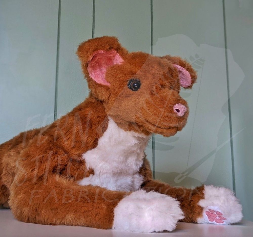 A photo of a handmade plush of a mutt. She's a golden brown with white socks and a white chest. The front half of her body is in view, with her legs outstretched, one paw rotated towards the viewer. Her paw pads are very pink. Her ears are the kind that stand up straight but flop down at the tip. She has a pink little nose.