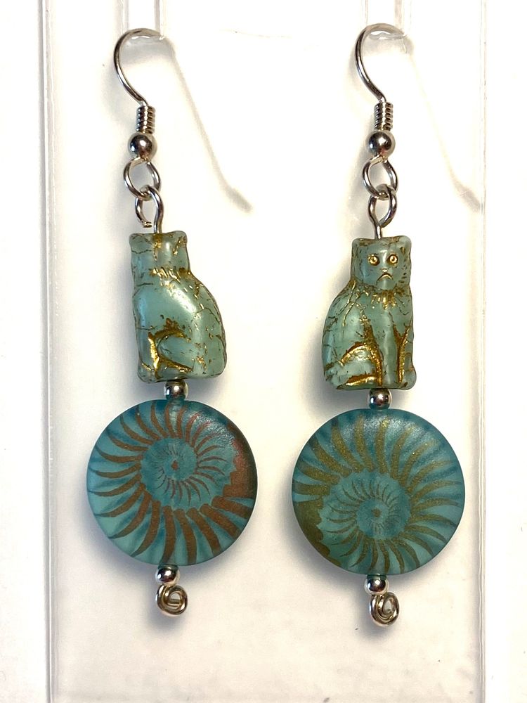 These sterling silver earrings feature two Czech glass beads on each. At the bottom is a big coin bead of matte aqua glass with a bronze-toned finish etched into an elaborate spiral. At the top is a glass cat in palest green-blue with golden finish picking out the cat's features. See the video for how the cat bead is in 3D. All the metal here is sterling silver.