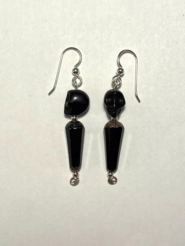 These sterling silver earrings feature a dyed black magnesite skull bead at the top and an inverted faceted Czech glass teardrop in jet black with picasso finish on the ends. The inverted teardrops are about twice as tall as the skull beads, giving the earrings a sleek almost Art Deco silhouette.