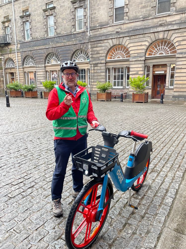 Photo of Chas Booth on a Dott e-bike in the quadrangle at Edinburgh City Chambers. 
