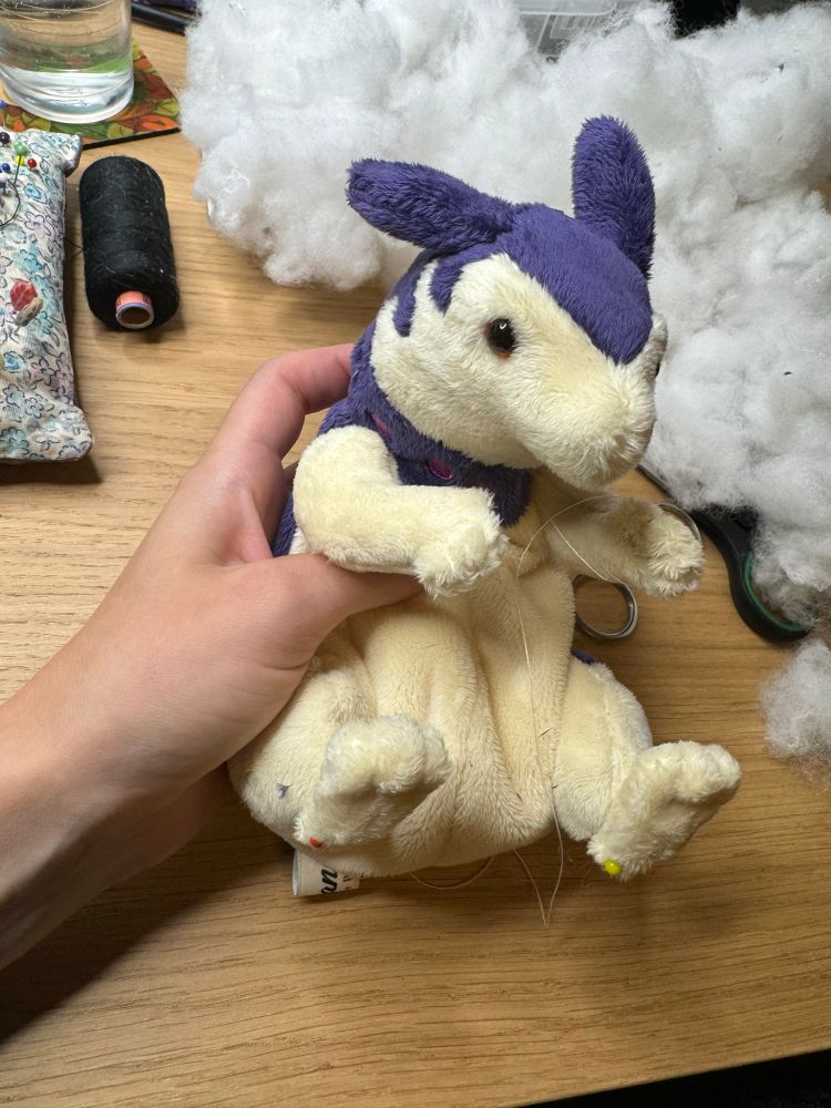 Work in progress hisuian typhlosion plushie held tightly in a hand. It does not have a face yet aside from eyes and the feet are on with pins. It kind of reminds of a pet rat