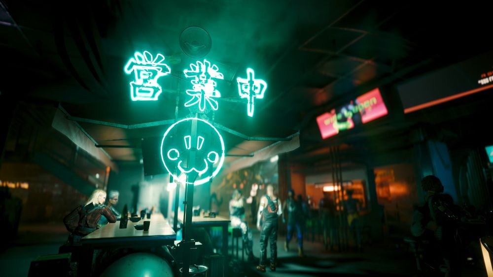 A view of an area of the black market in the Petrochem Stadium. Many people roam in the background and an advertisement screen can be seen to the top right.

To the centre-left, and foreground of the picture, there's a food stall with bright, green-ish neon depicting a smiley face and Chinese script. There is smoke all around, it's very busy.