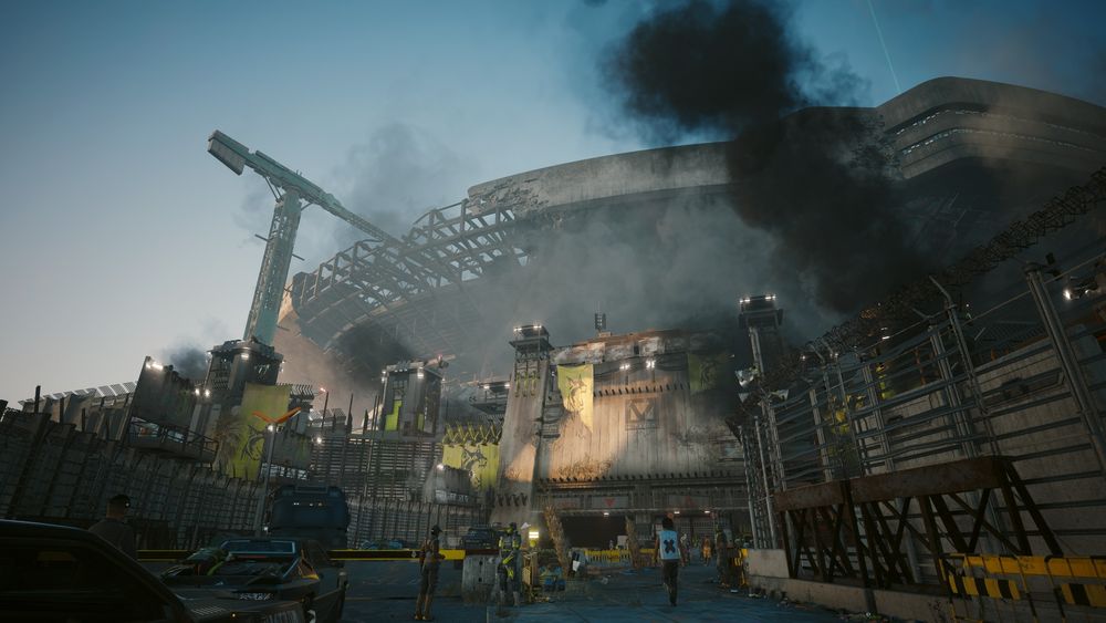 A picture of the derelict Petrochem Stadium in Cyberpunk 2077, showing the main entrance to Dogtown, the enclave within Night City. 

The stadium is gigantic and half-destroyed on top, with a crane towering over it. At the bottom, thick dark smoke towers into the sky, whereas the rest of the scene is covered in thinner and lighter smoke. 

There is a security checkpoint full of guards wearing yellow and black military gear, and with yellow banners hung from walls, depicting a dog.