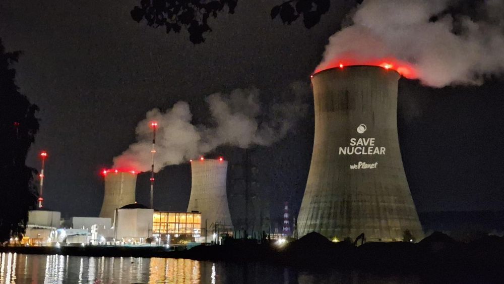 The tihange nuclear plant in Belgium at night. A projector displays the phrase “SAVE NUCLEAR weplanet” on the cooling tower
