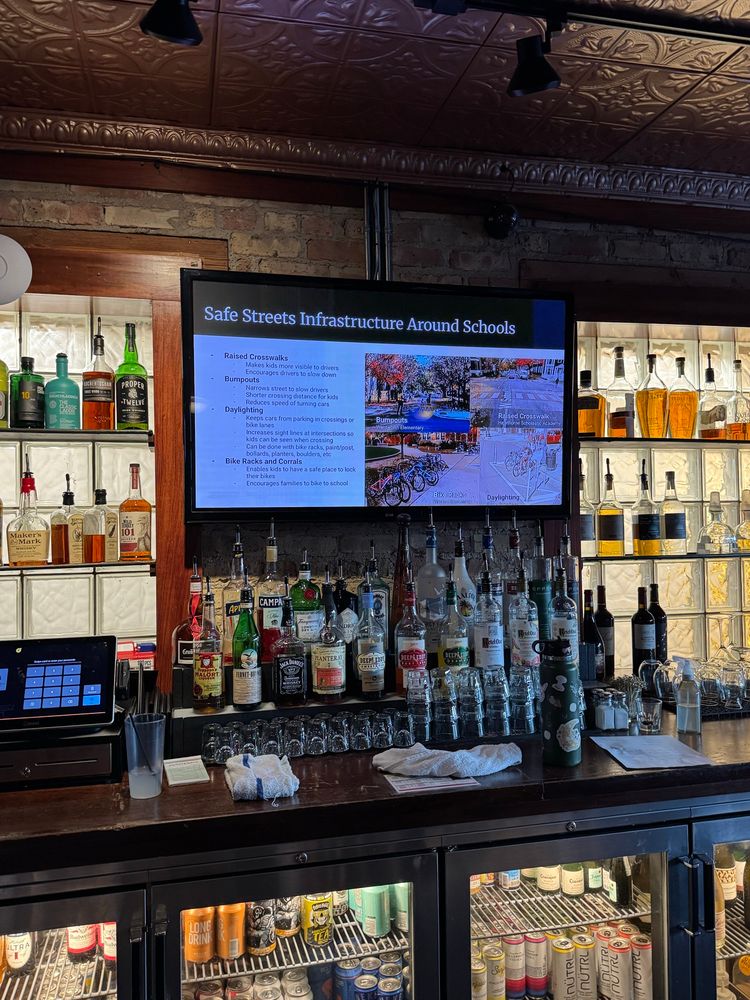 A screen says “safe streets infrastructure around schools” over a bar