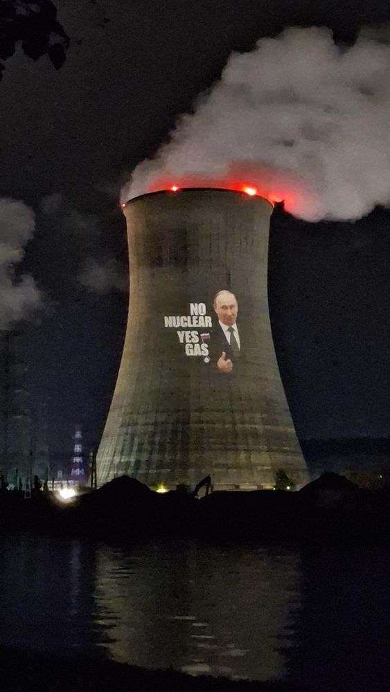 The tihange nuclear plant in Belgium at night. A projector displays the phrase “No Nuclear Yes Gas” on the cooling tower with a photo of Putin 